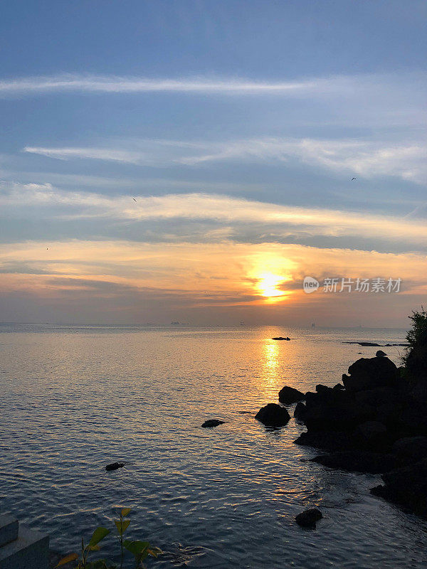 令人惊叹的印度果阿海滩的图像与橙色的日落天空，大海，云彩和日出/日落海岸线的倒影在多纳宝拉海滩照片，果阿，印度南部，岩石的剪影，沙子，涟漪拍打海岸和反射着明亮的橙色太阳